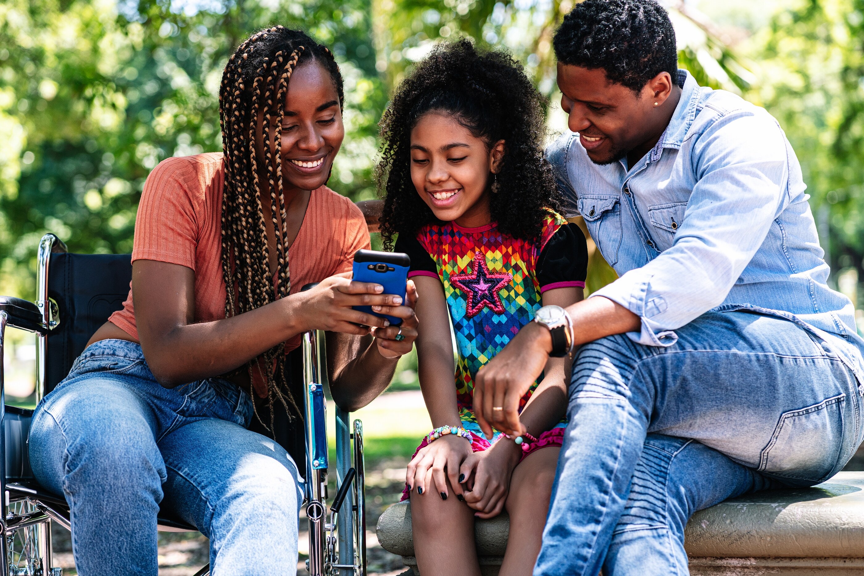 A family sharing something funny on a phone in the park, the mother in her wheelchair