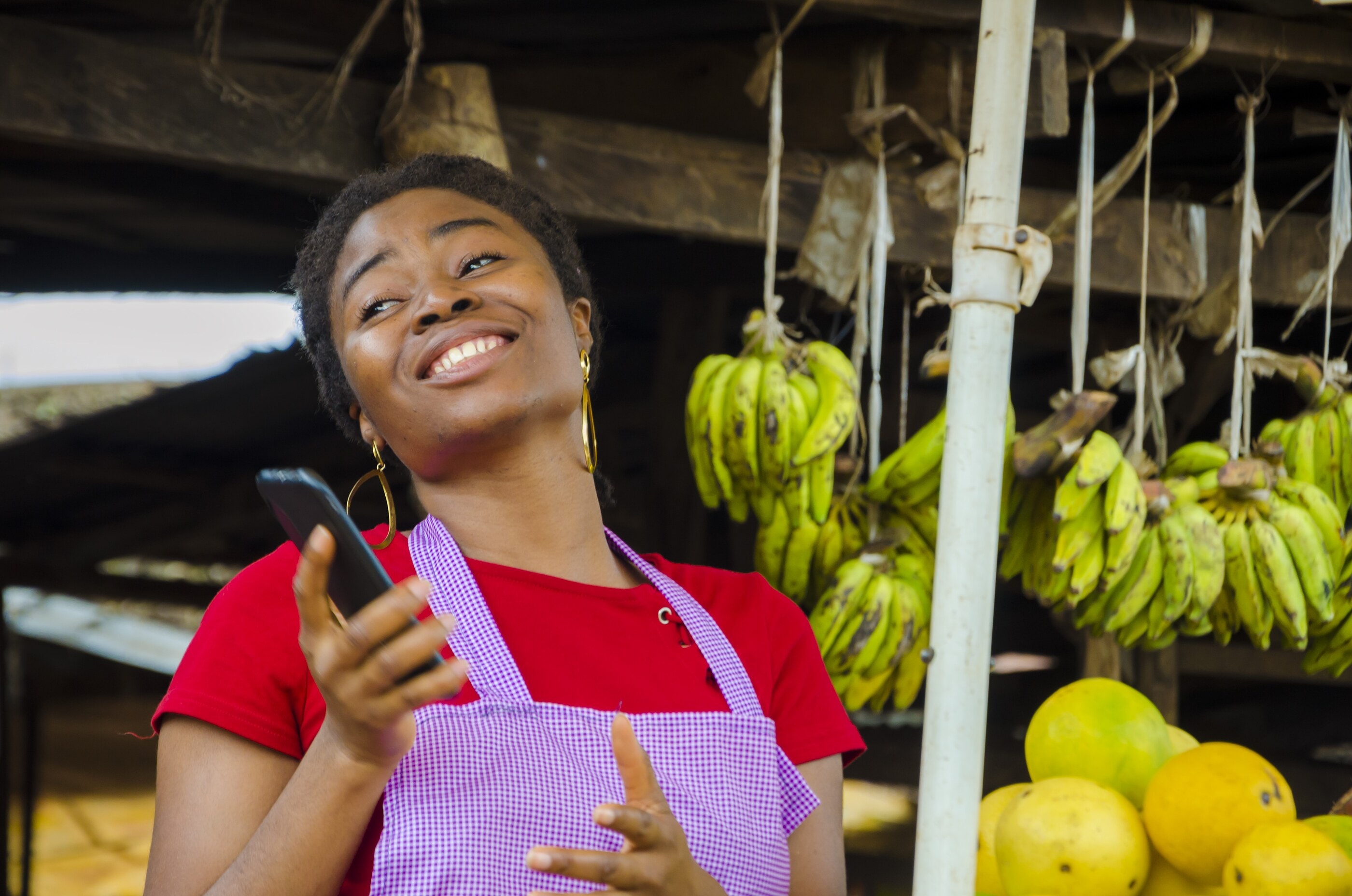 A market trader at her plantain stall, delighted by a message on her phone